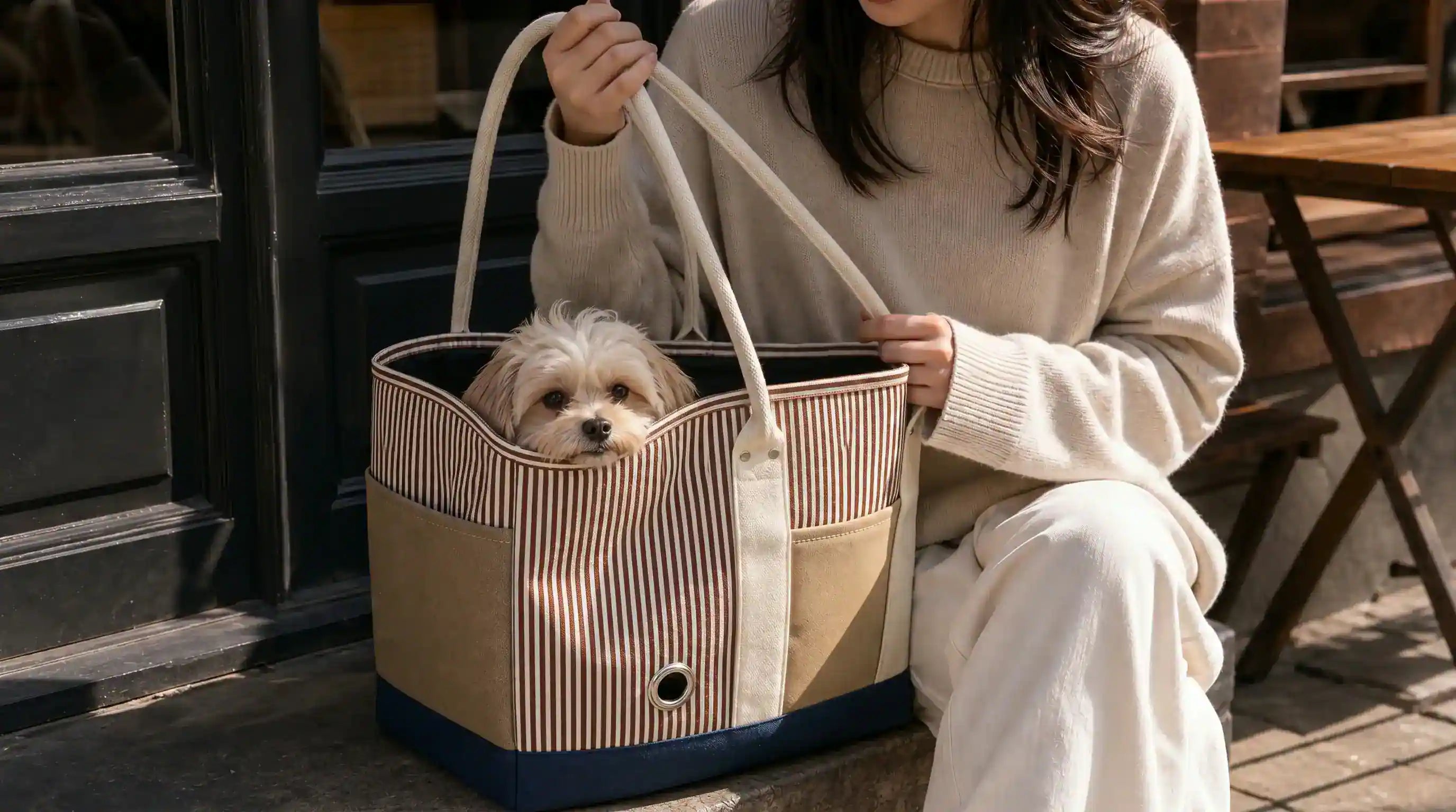 small dog resting in a tote style carrier bag near a cafe table