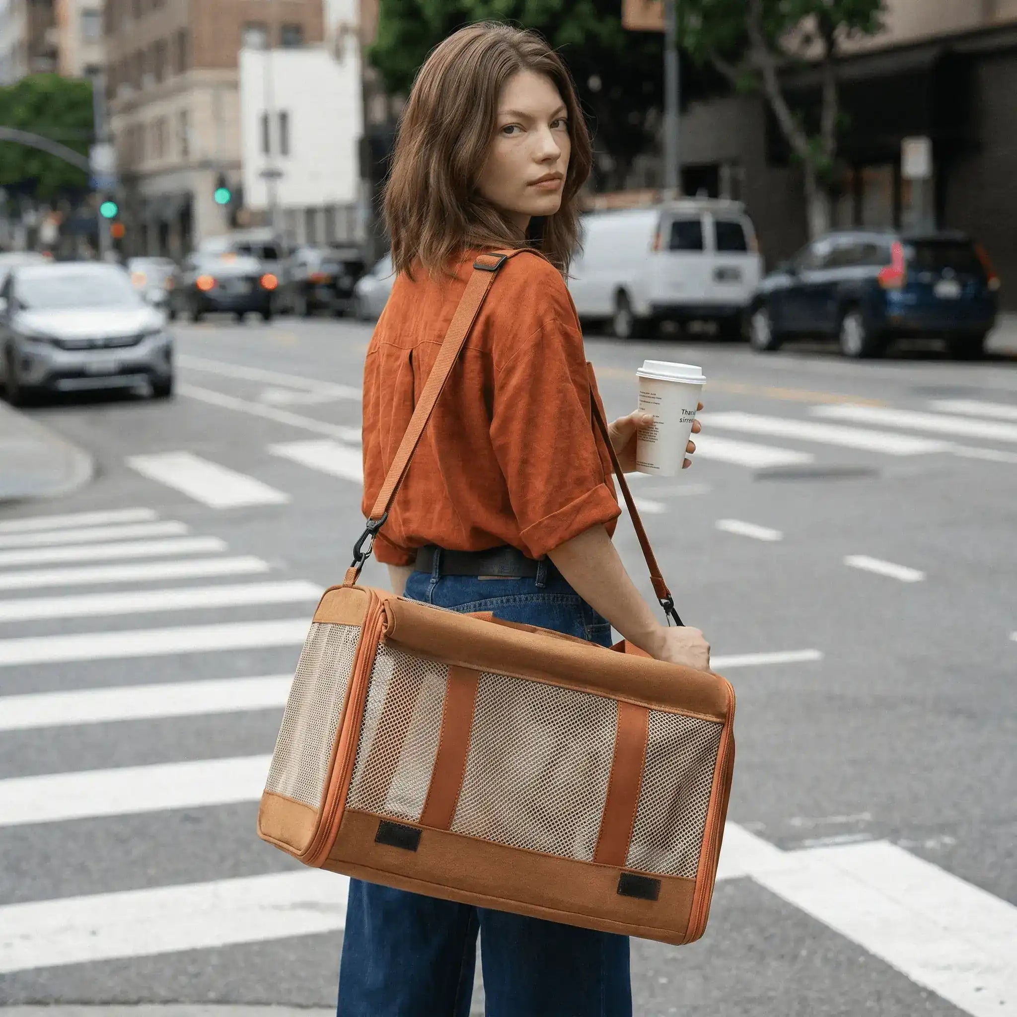 A model is carrying a pet carrier using a crossbody strap while on road