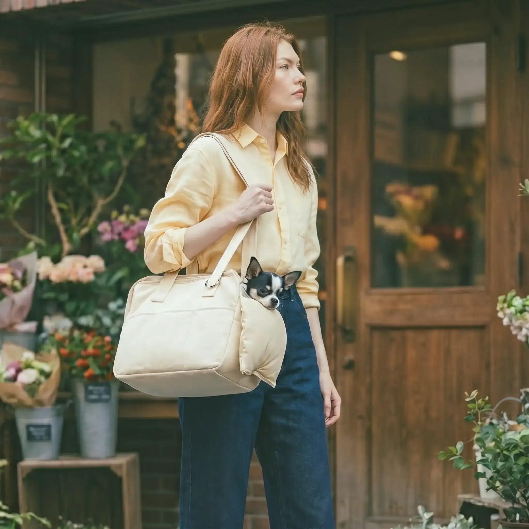 A model is wearing a beige pet tote bag over her shoulder with a Chihuahua inside