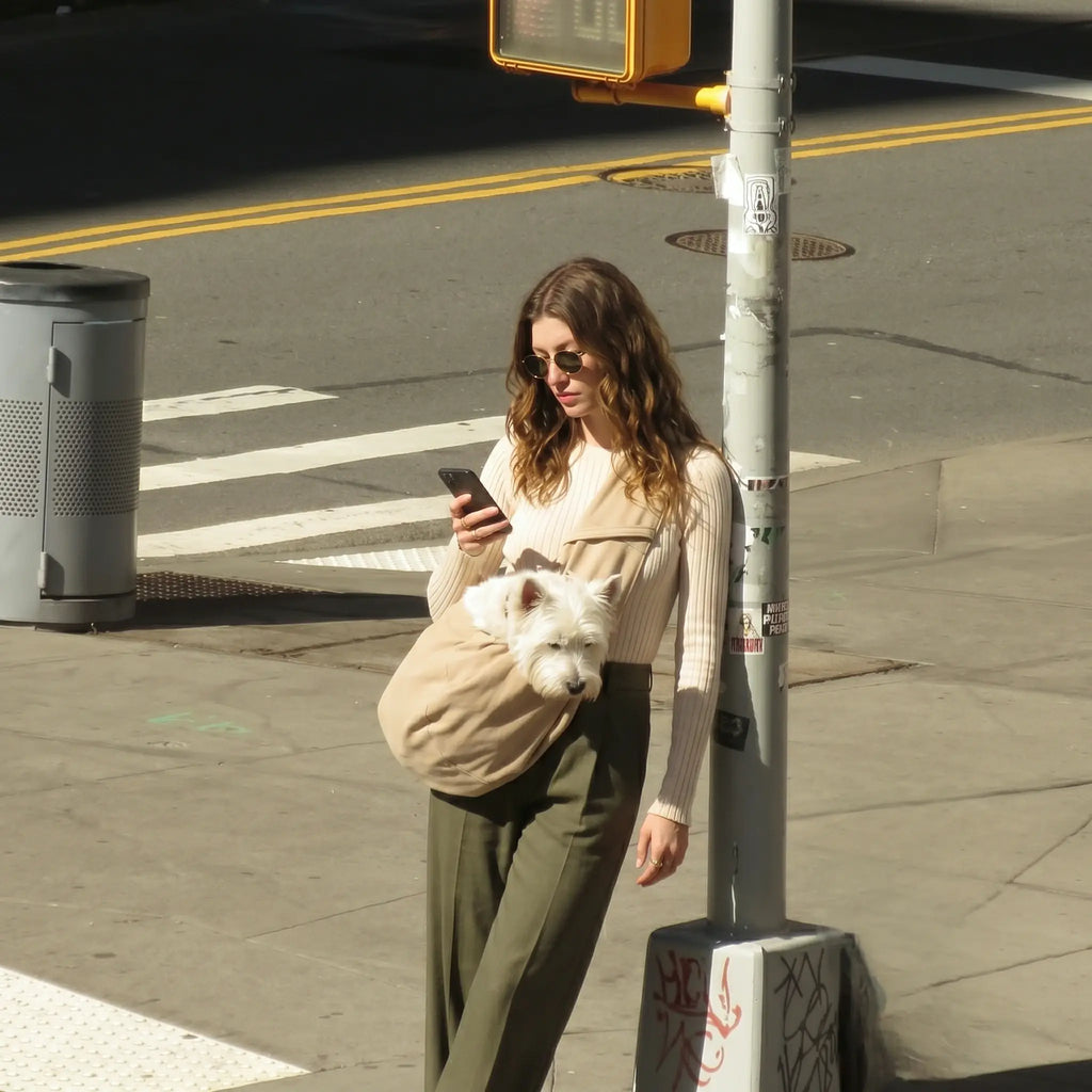 A woman with a pet in a crossbody carrier bag leaning against a railing 