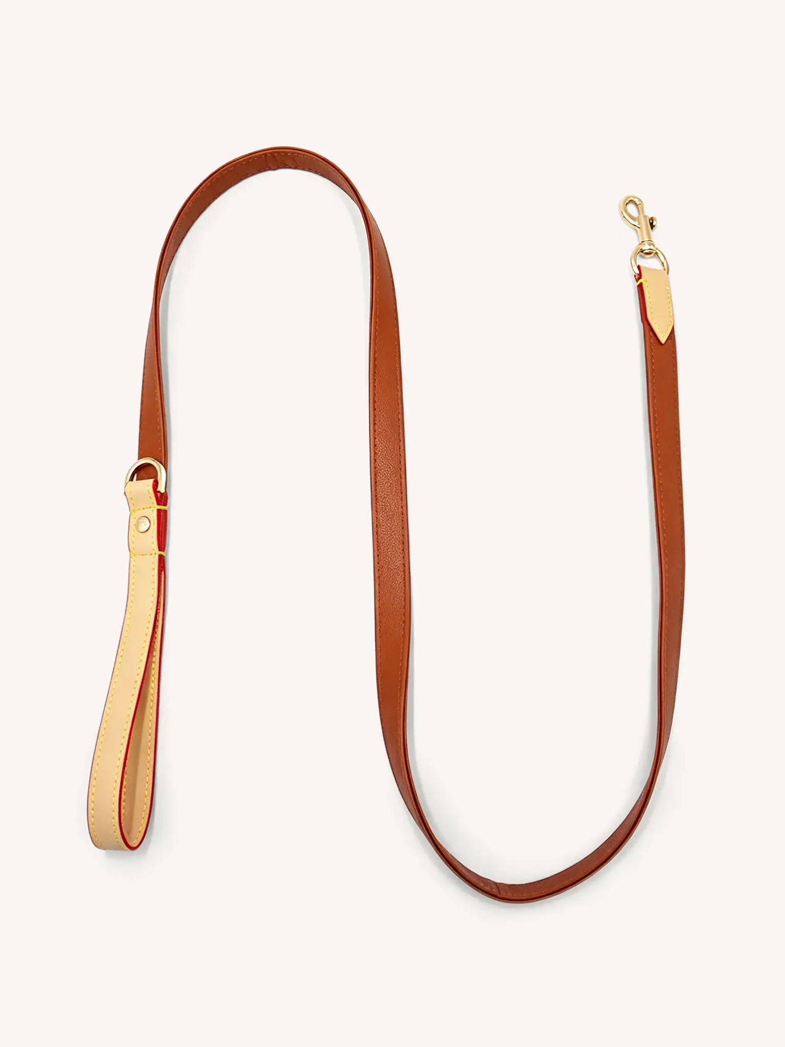 A brown leather leash with gold hardware is lying flat on the ground.